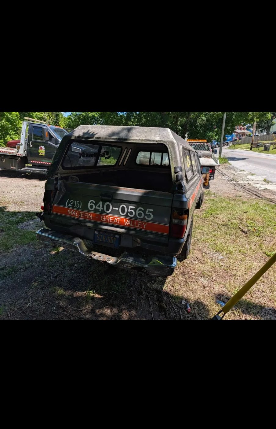 Rear of the Dodge D50 showing bed cap, bumper damage, and work lettering