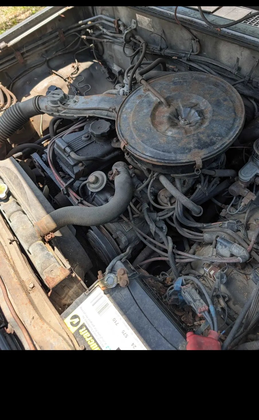 Engine bay of the 1988 Dodge D50 with battery and dusty carburetor air cleaner