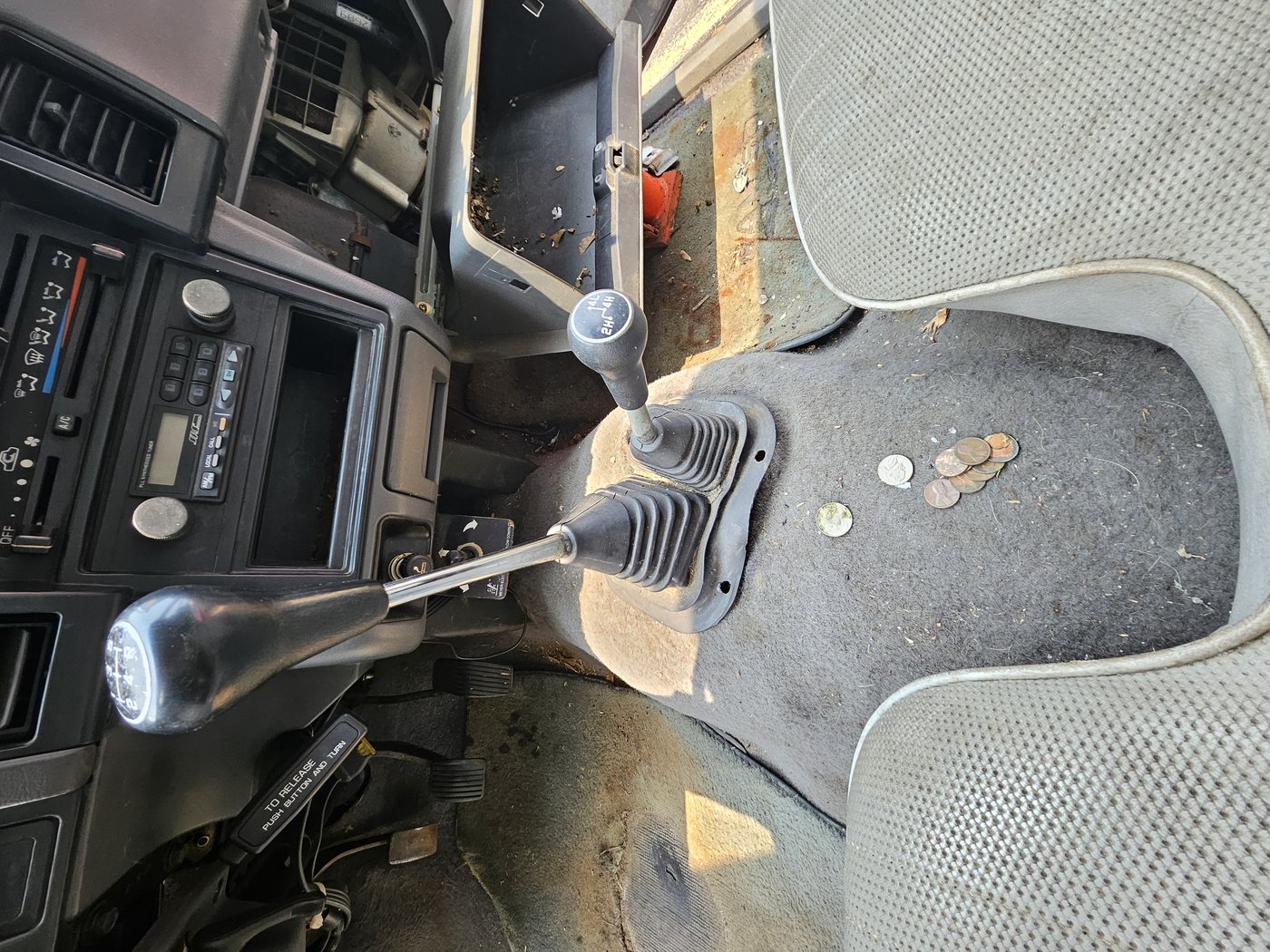 Five-speed and transfer case shifters in the D50 cab floor with debris and coins