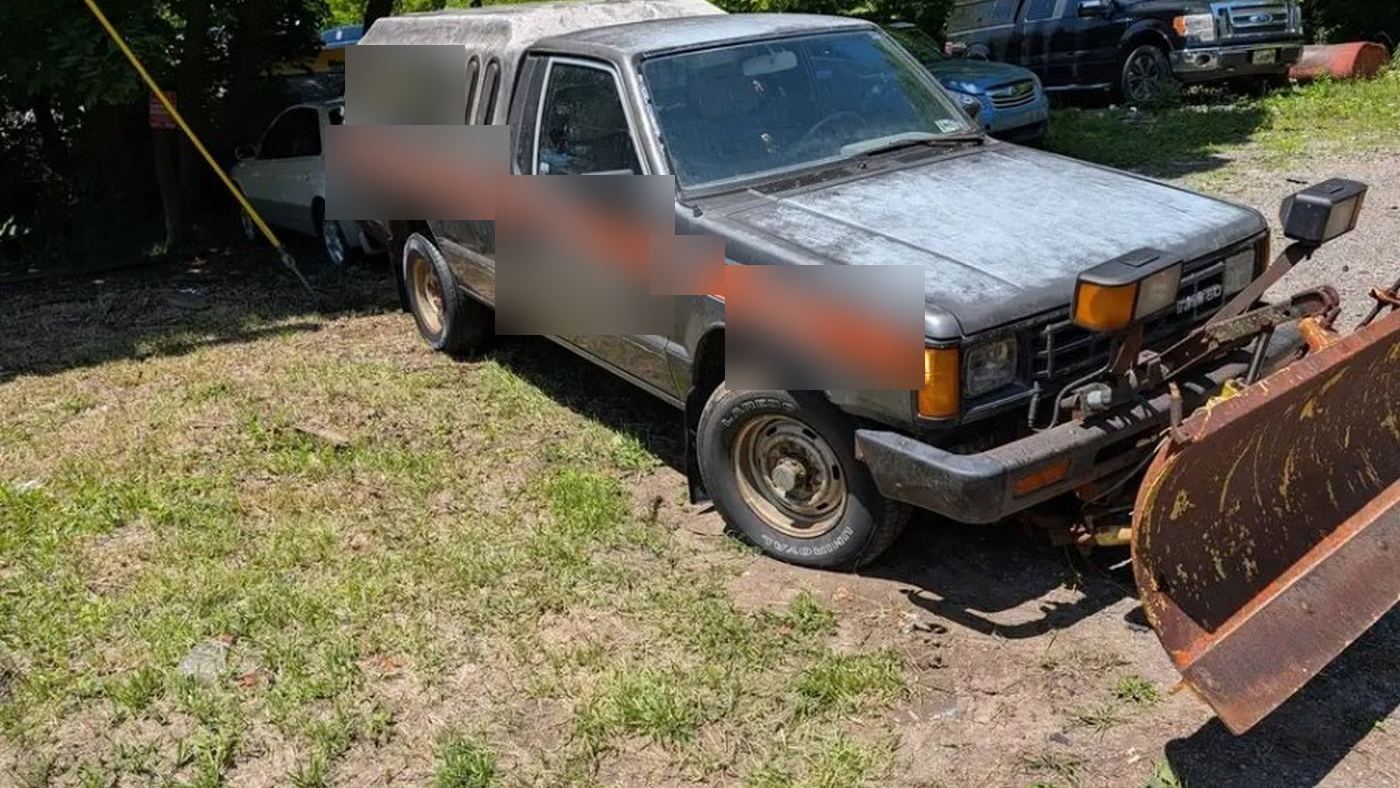 1988 Dodge D50 4x4 with rusted snow plow blade and bed cap, parked on grass after delivery